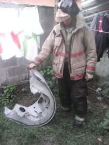 Un miembro del Cuerpo de Bomberos muestra la piea de la avioneta que cayó sobre una vivienda en Ls Lims.