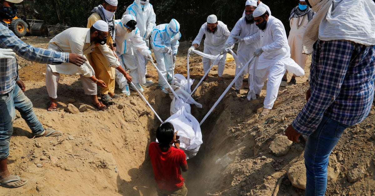 People lower the body of a man who died from COVID-19 into a grave, at a graveyard in New Delhi