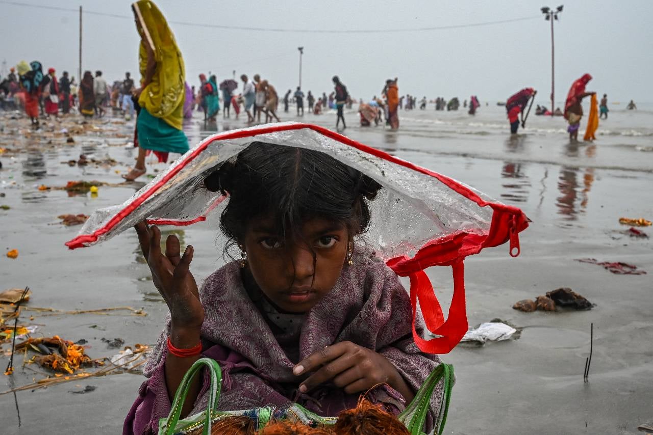 Una niña se cubre la cabeza con una bolsa de plástico para protegerse de la lluvia durante el Gangasagar Mela.