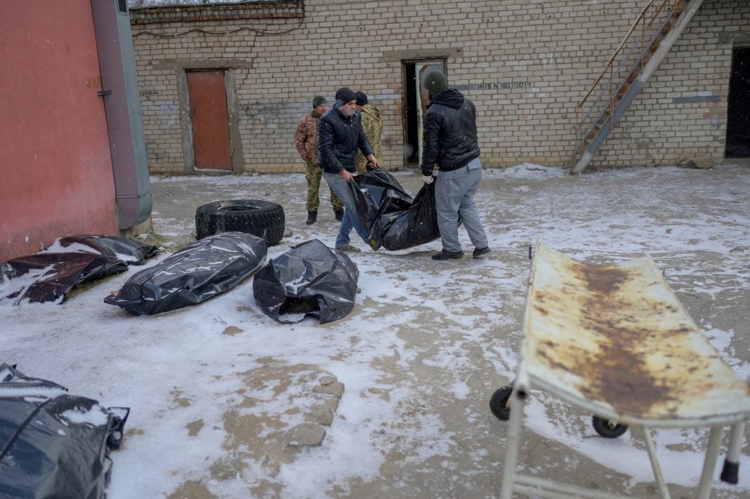 Dos hombres cargan un cuerpo en una bolsa para cadáveres para colocarlo junto a otros en un patio cubierto de nieve.