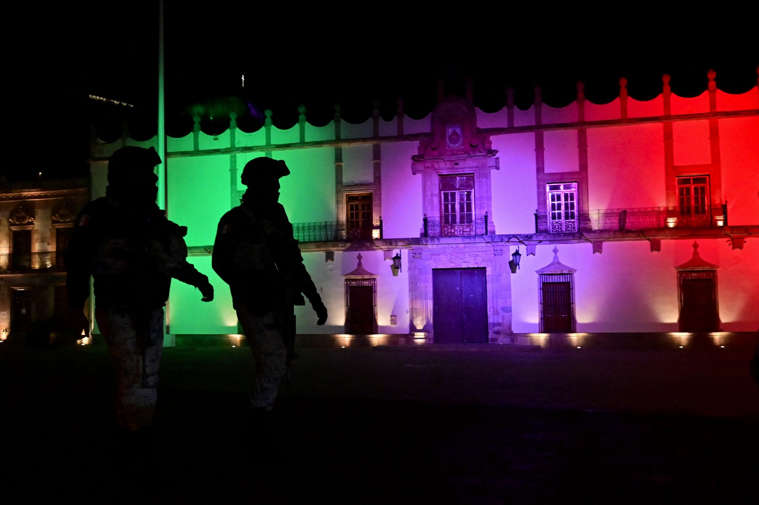 Los miembros de la Guardia Nacional pasan por el edificio del Palacio de Gobierno iluminado con los colores de la bandera mexicana.