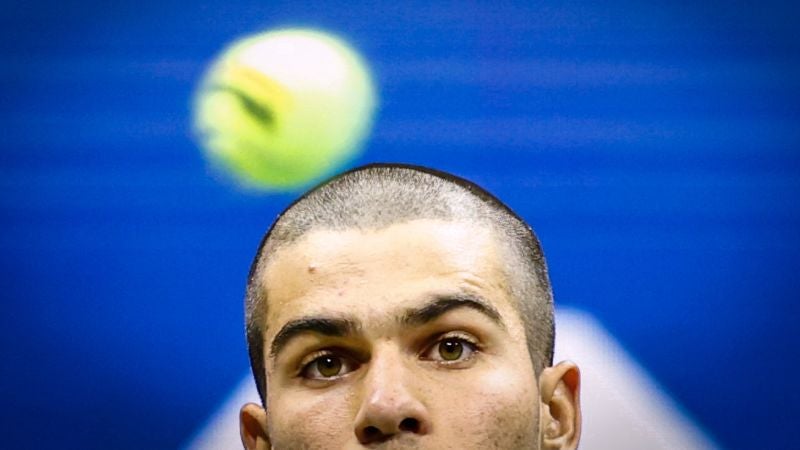 El español Carlos Alcaraz mira la pelota durante su partido de primera ronda de individuales contra el estadounidense Reilly Opelka.